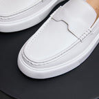 Men's white leather slip-on sneaker close-up with stitched moc toe and textured sole edge.