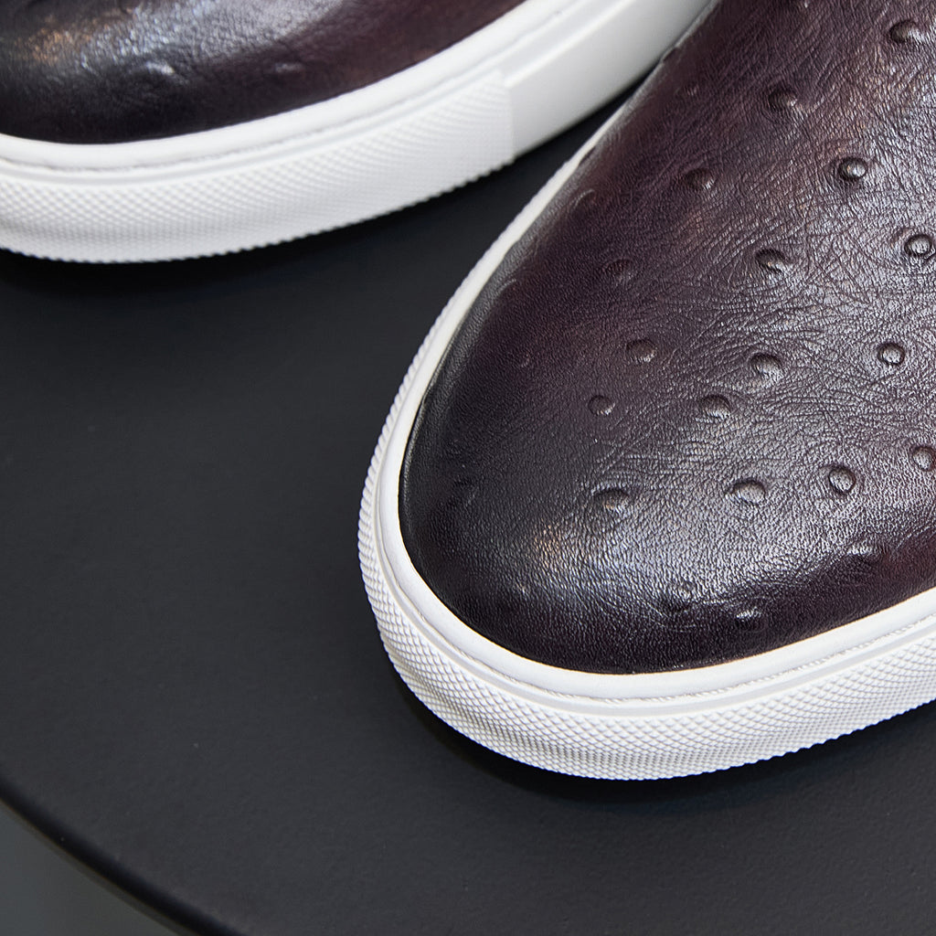 Close-up of dark leather sneaker toe with perforated pattern and white rubber trim