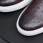Close-up of dark leather sneaker toe with perforated pattern and white rubber trim