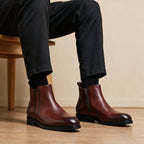 Pointed-toe leather side-zip dress boots in brown, side view with cuffed jeans