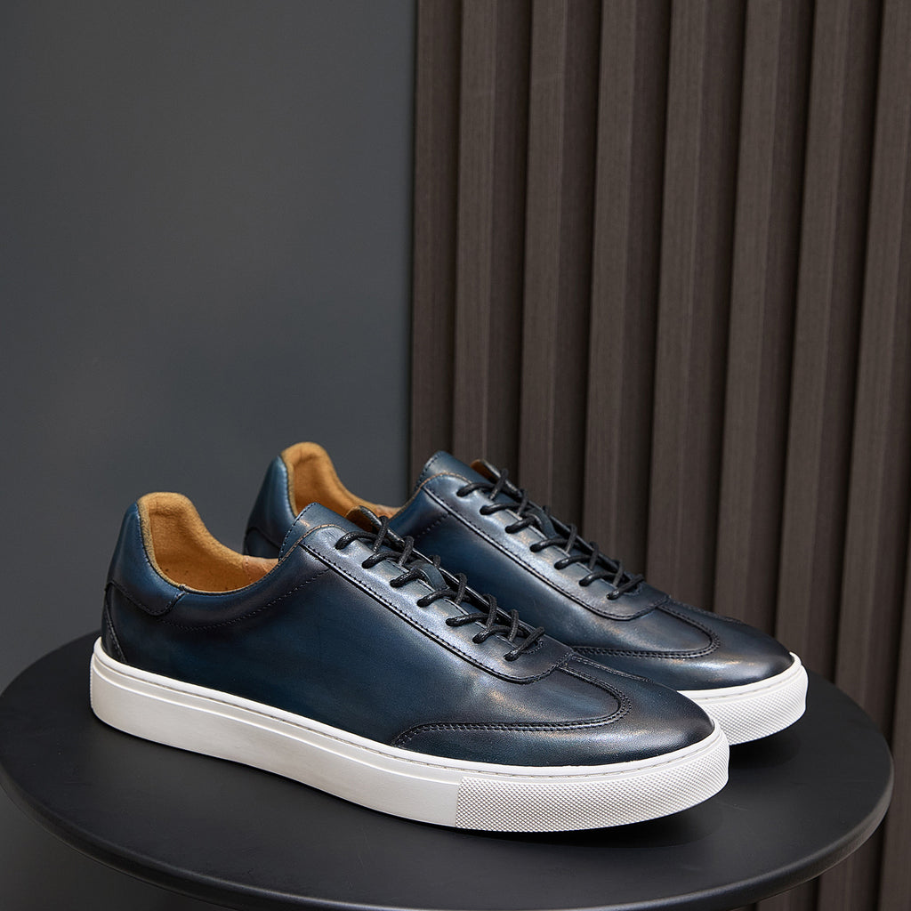 Men's leather sneakers in blue with black laces, white sole, and tan lining.