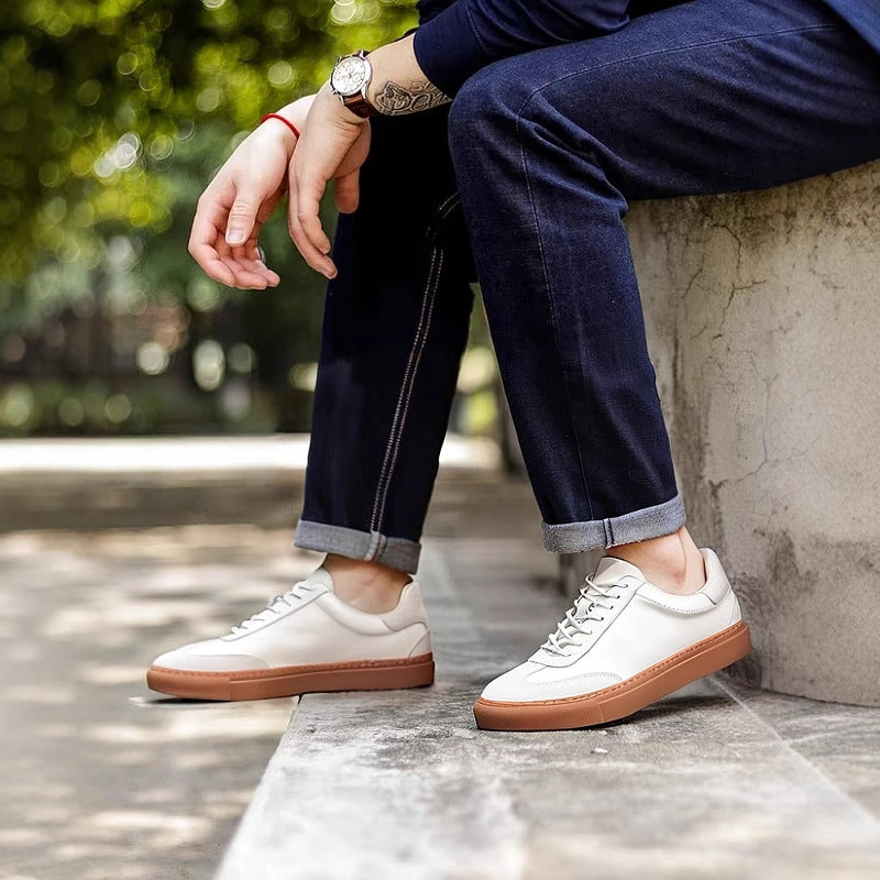 White leather lace-up sneakers with tan sole, worn with dark jeans