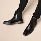 Black leather Chelsea boots worn with black pants, elastic side panels