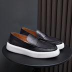 Pair of black leather slip-on sneakers with moccasin stitching and white platform sole
