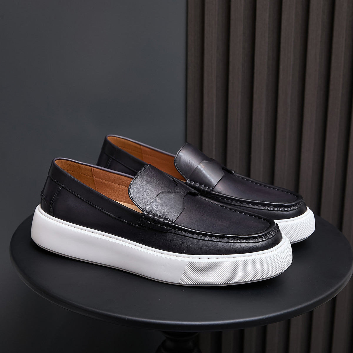 Pair of black leather slip-on sneakers with moccasin stitching and white platform sole
