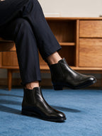 Black pointed-toe chelsea boots with elastic side panels, worn with rolled pant cuffs