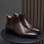 Dark brown pointed-toe Chelsea dress boots with elastic side panels and flat sole