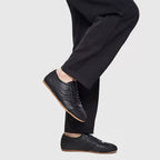Men's black leather sneakers on feet; lace-up front and gum-style sole