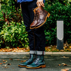 Brown leather lace-up ankle boots with side-zip, worn outdoors while lifting one foot.