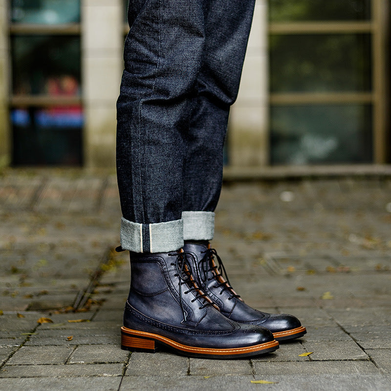 Men's dark leather lace-up chukka boots with perforated toe, worn with jeans cuffs