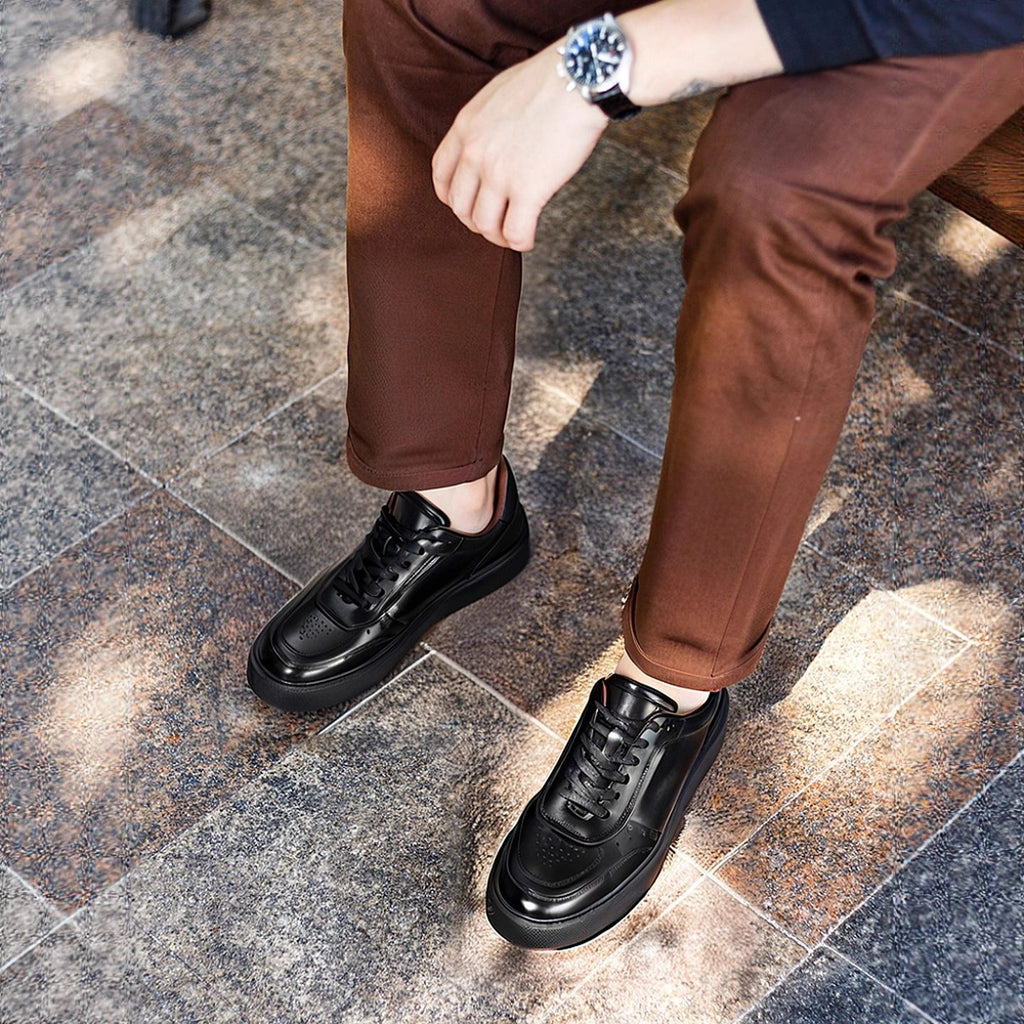 Black lace-up leather sneakers with rounded toe and thick rubber sole, shown on feet.