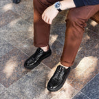 Black lace-up leather sneakers with rounded toe and thick rubber sole, shown on feet.