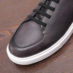 Black genuine leather sneaker with lace-up straps and rounded toe, white rubber sole.