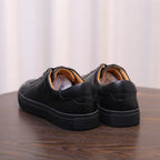 Black leather sneakers showing heel and back panel with tan lining and seams.