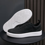 Black leather sneakers with textured white outsole, minimalist low-top profile.