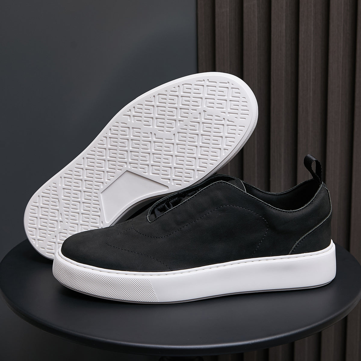 Black leather sneakers with textured white outsole, minimalist low-top profile.