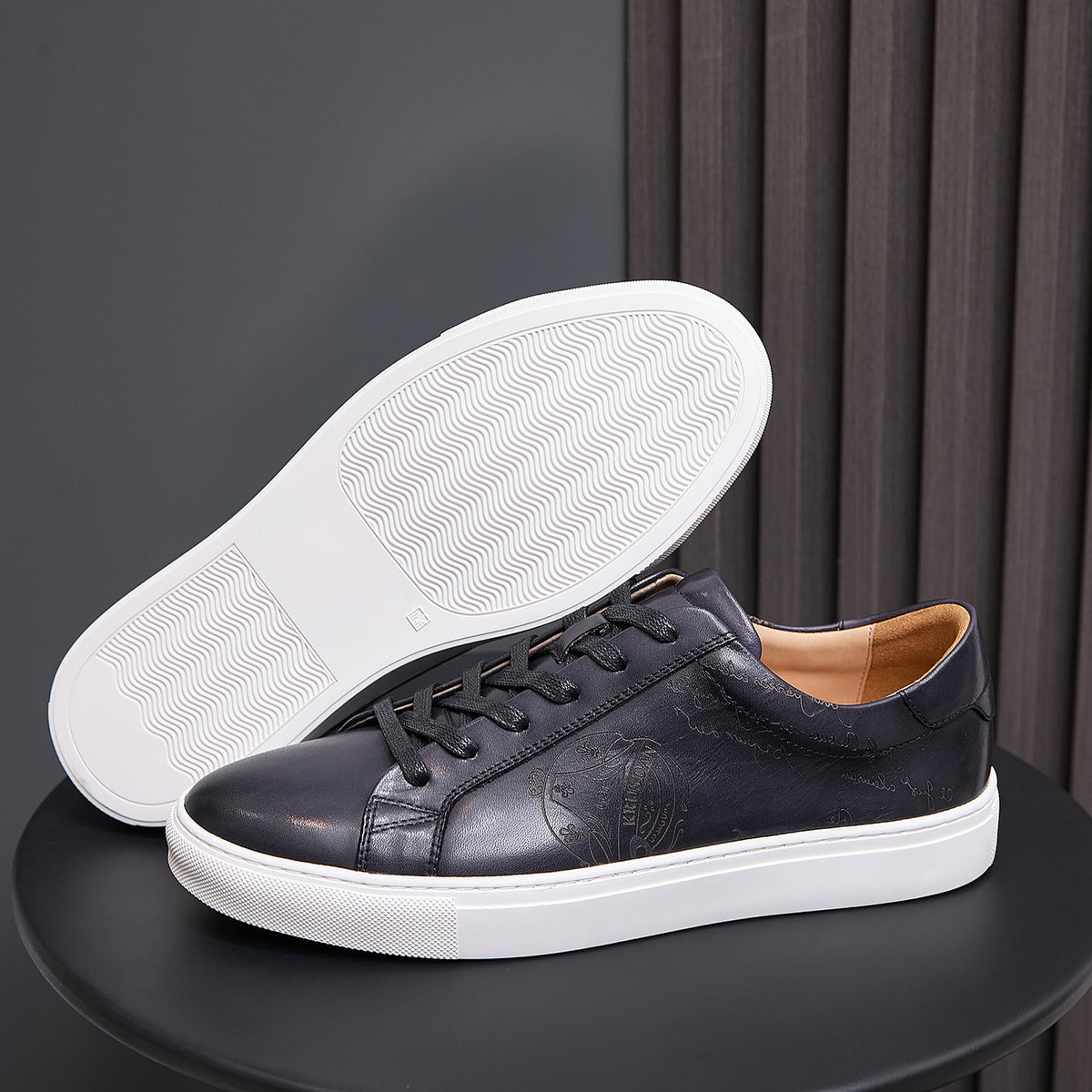 Black leather sneaker showing white treaded outsole with lace-up upper
