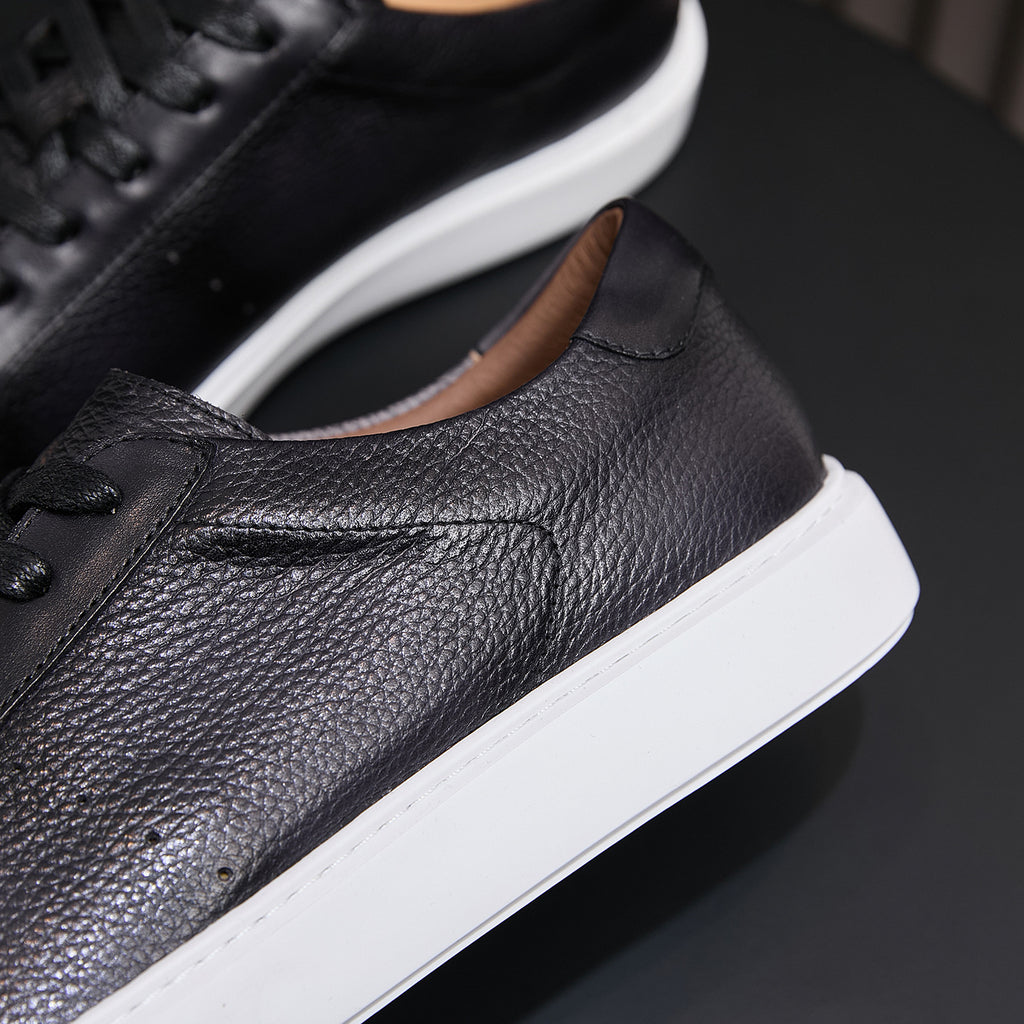 Black leather sneaker side with smooth stitching, cushioned collar, and white sole
