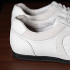 White leather sneaker side profile with cushioned collar and dark rubber sole.