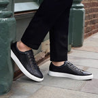 Black leather lace-up sneakers worn with dark pants and white rubber soles.