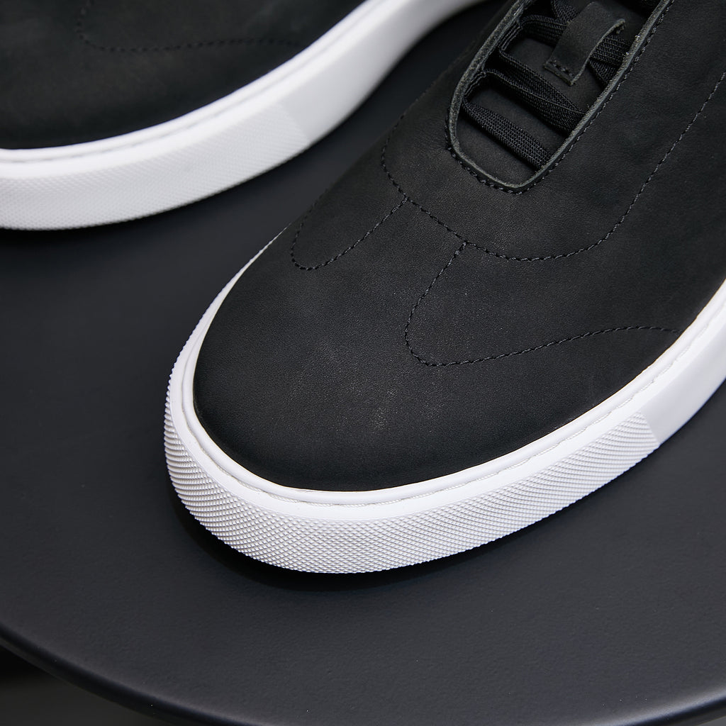 Black leather sneakers with lace-up top panel and white rubber midsole.