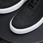 Black leather sneakers with lace-up top panel and white rubber midsole.