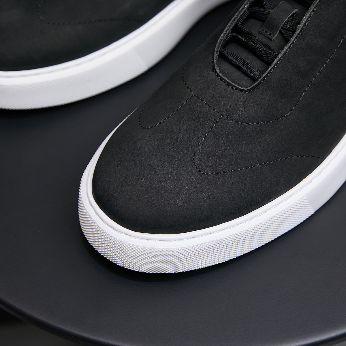 Black leather sneakers with lace-up top panel and white rubber midsole.