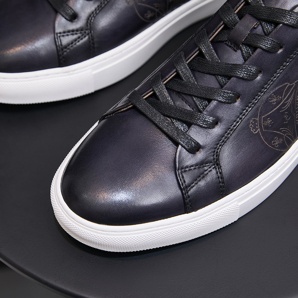 Black leather lace-up sneaker close-up with detailed stitching and white rubber sole