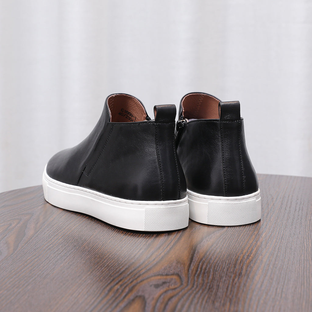Black leather side-zip ankle boots with white rubber soles, rear view