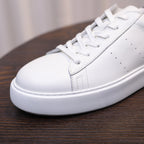 Close-up of white leather sneaker with laces, perforated detail, and textured side sole.