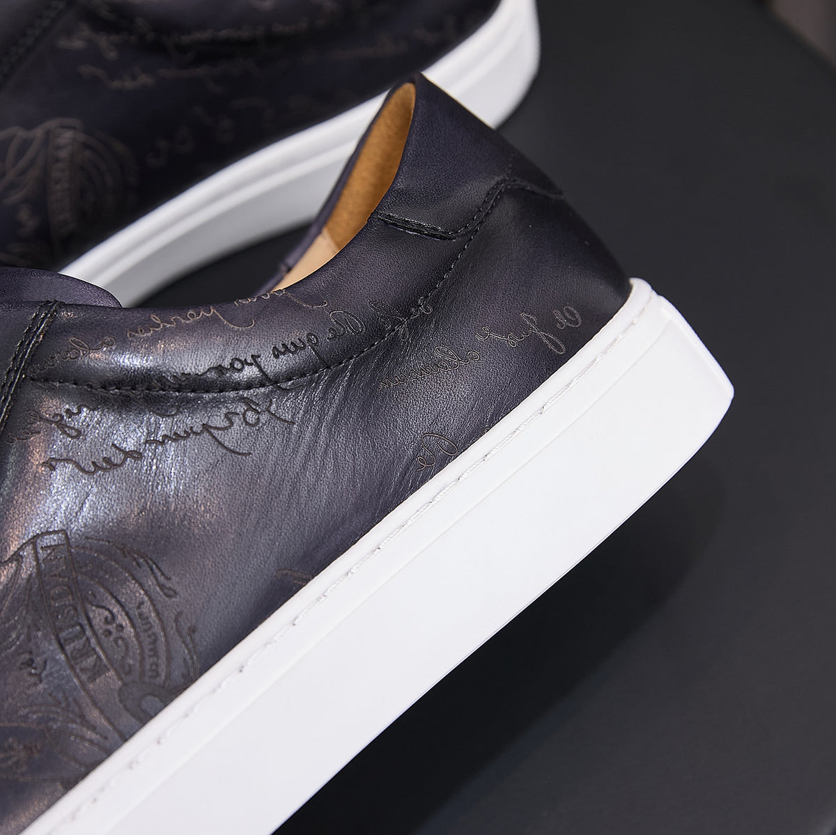 Black leather sneaker heel close-up with white sole edge and tan inner lining