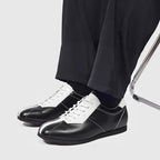 Black leather sneakers with white trim, lace-up closure, and rounded toe cap.