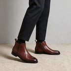 Pointed-toe leather side-zip dress boots in brown, front view with dark pants