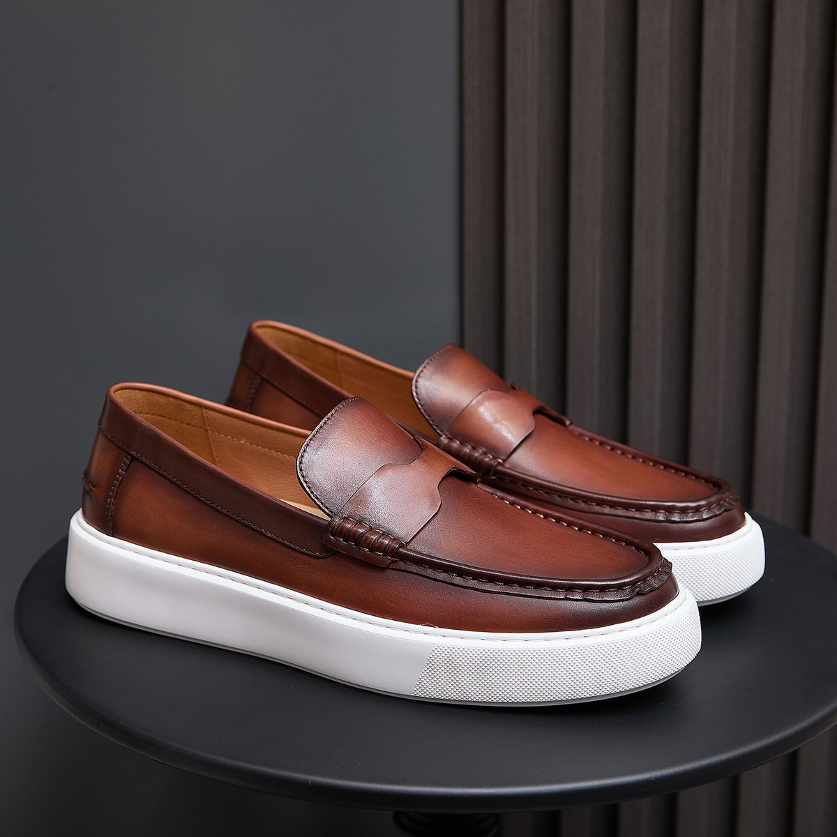 Pair of brown leather slip-on sneakers with moccasin stitching and white platform sole