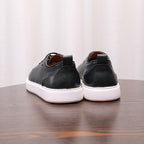 Pair of black genuine leather sneakers, heel and back profile with white rubber soles.