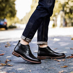 Black leather lace-up chukka boots on sidewalk, plain toe and stacked rubber sole.