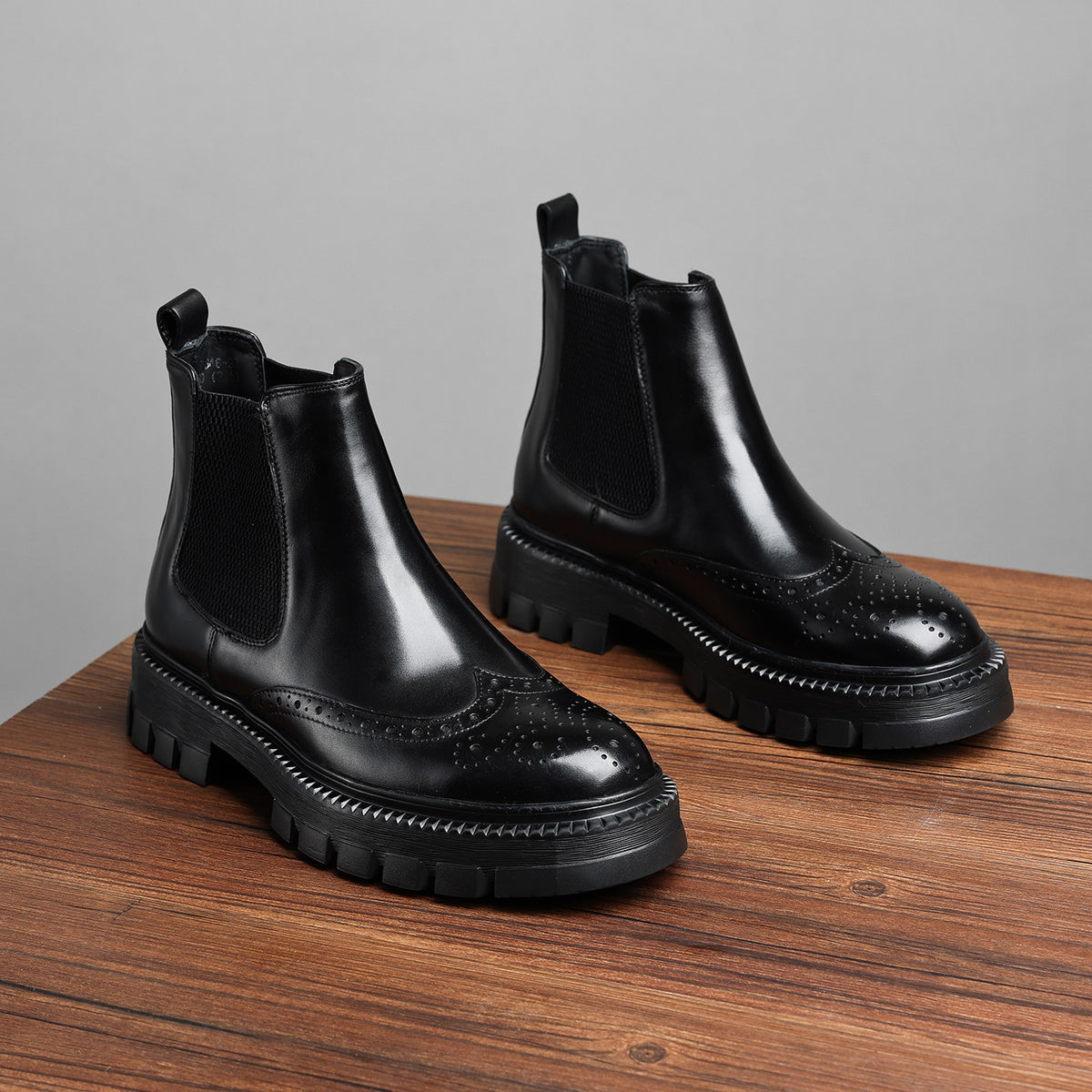 Black leather chelsea dress boots with elastic gore and wingtip brogue perforations, lug sole