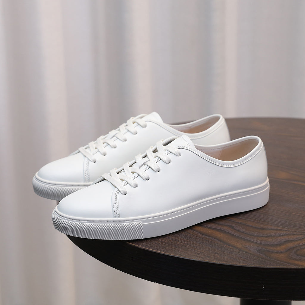 Men's leather sneakers, white low-top with lace-up front and rubber sole.