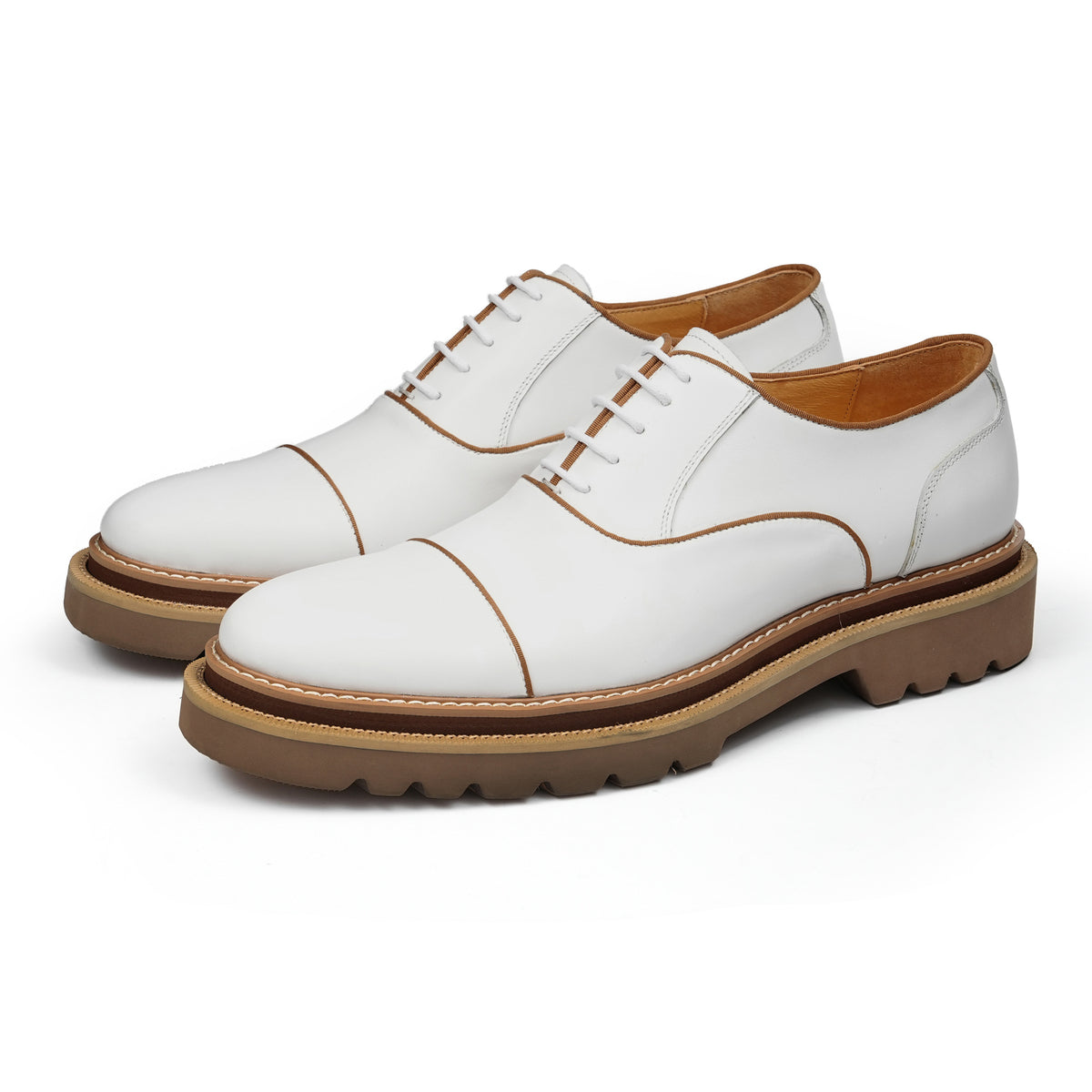 White lace-up oxford shoes with brogue/wingtip stitching and chunky lug sole.