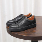 Men's black leather sneakers on a wooden table, lace-up with cushioned platform sole