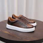 Dark brown leather low-top sneakers with lace-up front and white rubber sole.