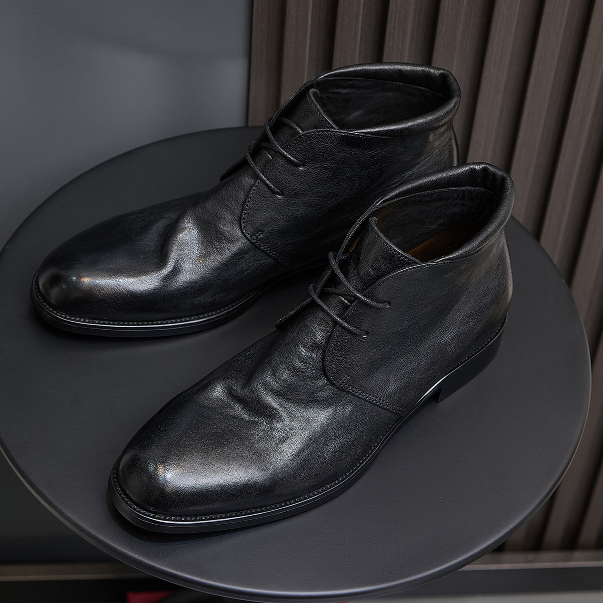 Black leather lace-up chukka boots, angled side view showing smooth plain toe.