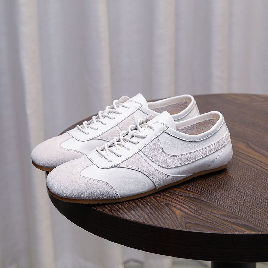 Men's white leather sneakers with lace-up front and padded collar on a table