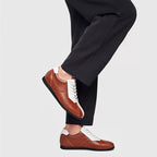 Brown leather sneakers with white laces, low profile sole, and side overlay panels.