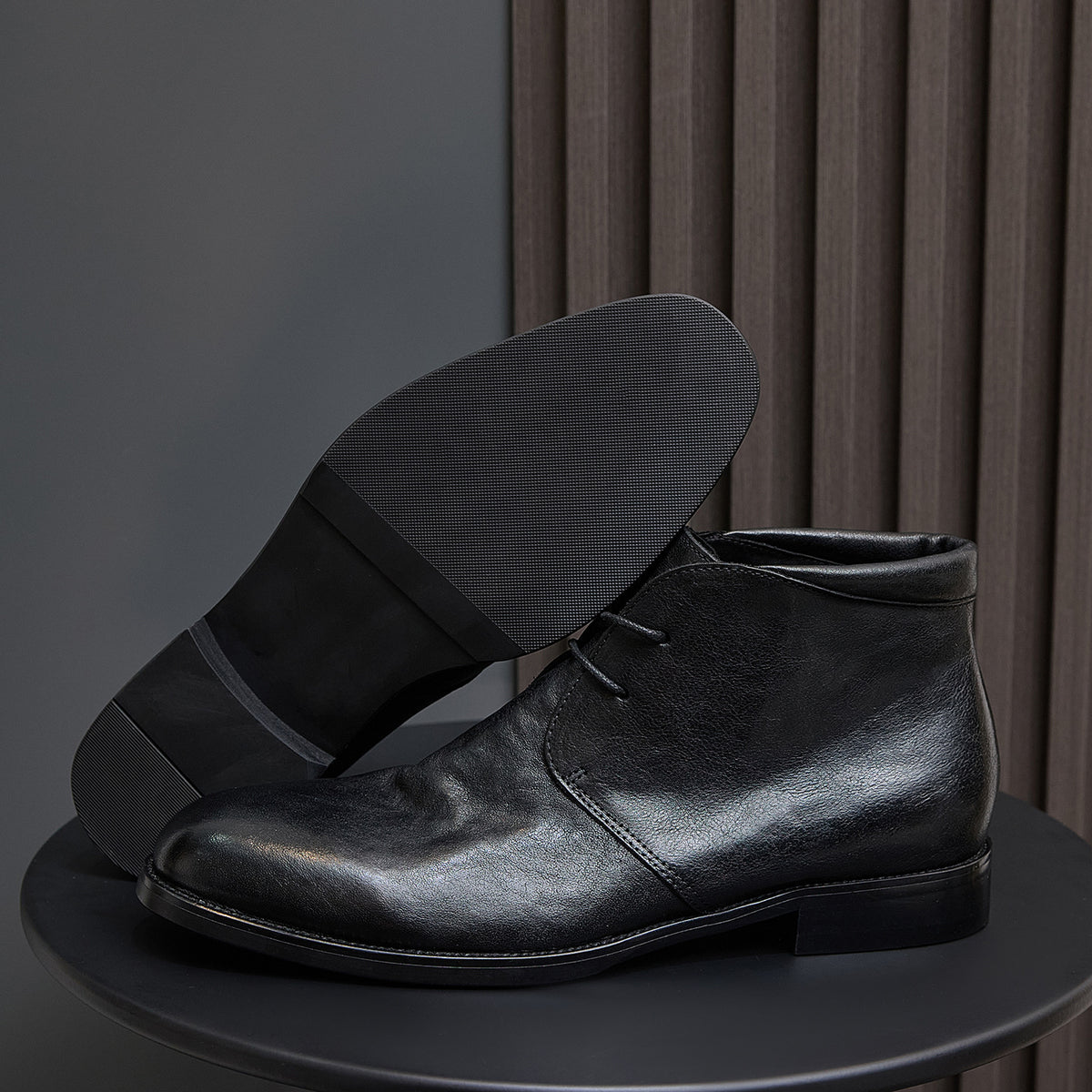Black leather lace-up chukka boot showing thick sole and stacked low heel.