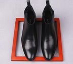 Black leather Chelsea boots with pull tabs and elastic gore on orange tray
