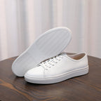 Men's leather sneakers, white with textured rubber outsole visible and lace-up upper.