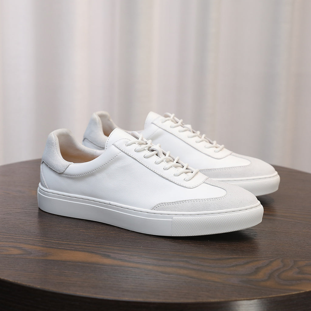 Men's white leather lace-up sneakers on a round wooden surface, minimalist design