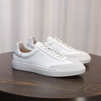 Men's white leather lace-up sneakers on a round wooden surface, minimalist design