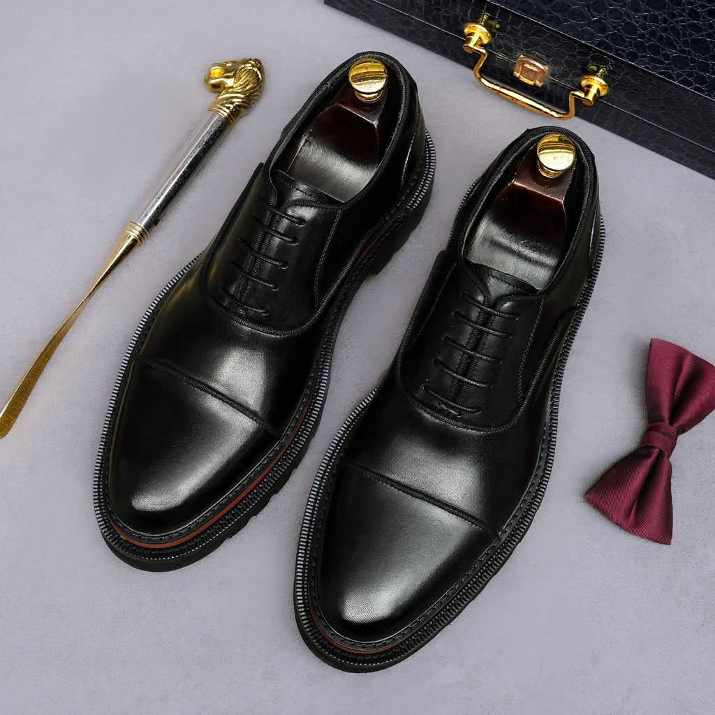 Black lace-up oxford shoes with brogue/wingtip stitching and chunky lug sole.
